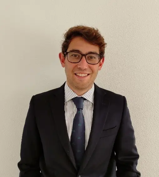 Hombre con traje y gafas sonriendo ante una pared clara