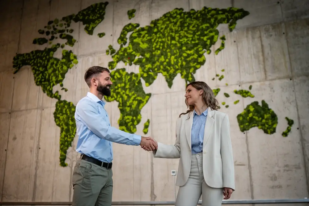 Dos profesionales estrechan manos ante mapa mundial verde